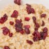 Close-up of creamy applesauce oatmeal in a white bowl, topped with chopped dried cranberries. Simple breakfast recipe; Weight Watchers cranberry applesauce oatmeal.