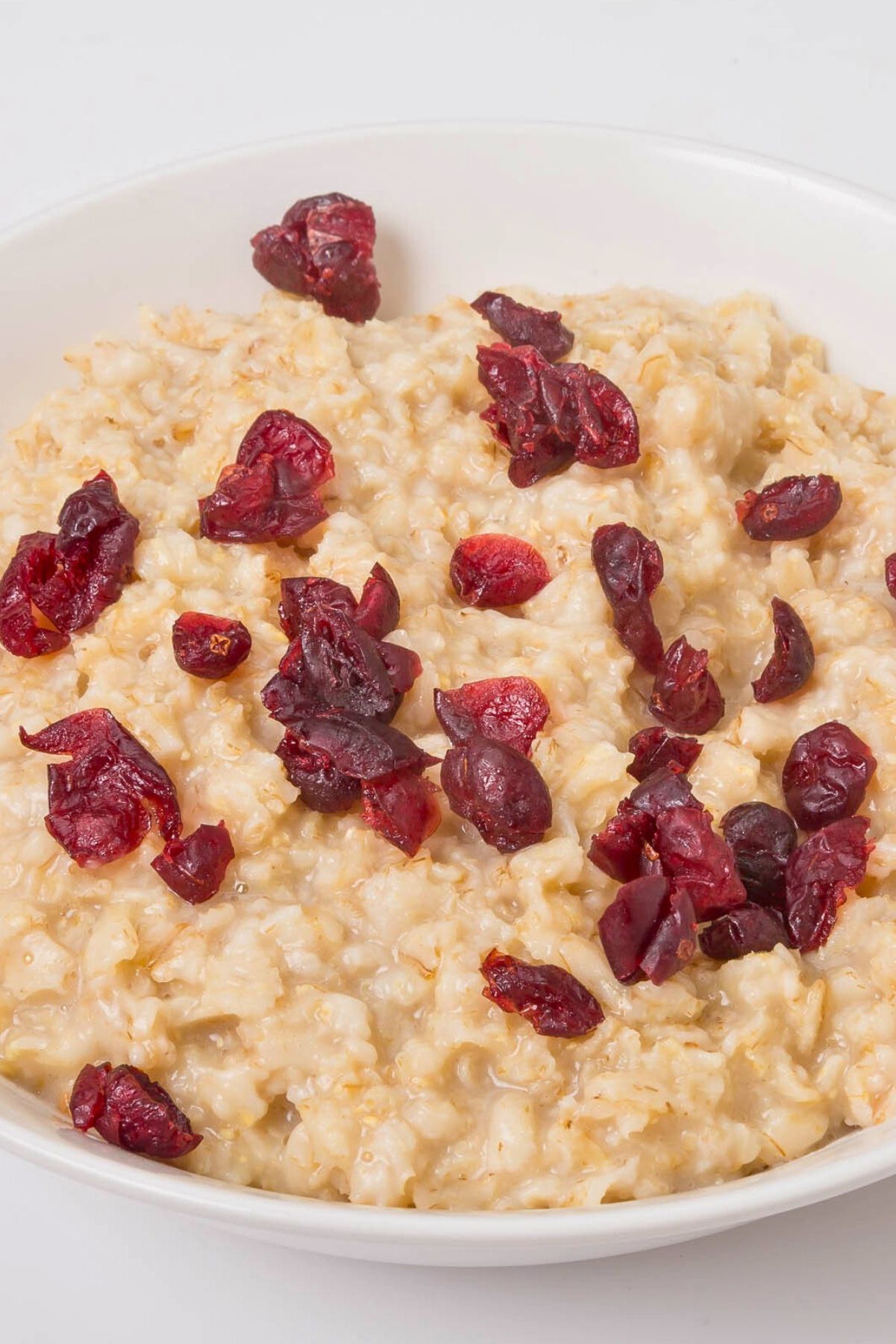 Close-up of creamy applesauce oatmeal in a white bowl, topped with chopped dried cranberries. Simple breakfast recipe; Weight Watchers cranberry applesauce oatmeal.