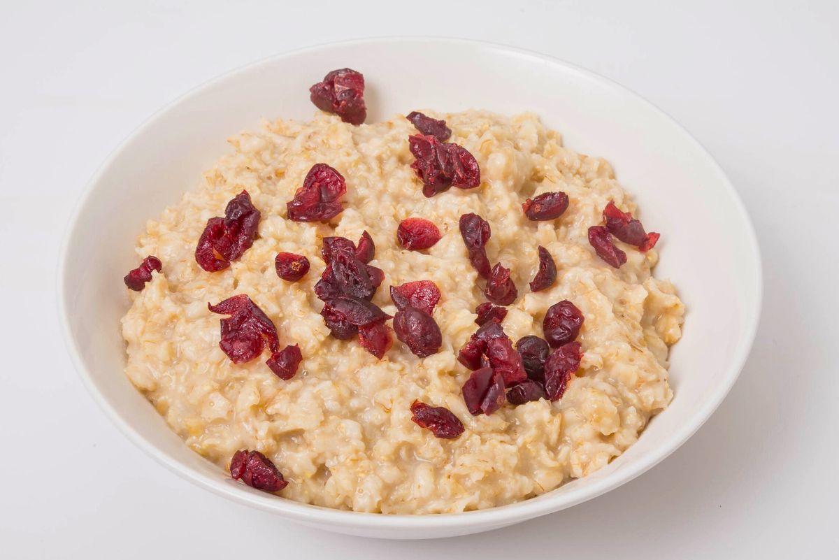 A white bowl filled with creamy oatmeal mixed with applesauce and topped with dried cranberries. Simple breakfast dish; Weight Watchers cranberry applesauce oatmeal recipe.