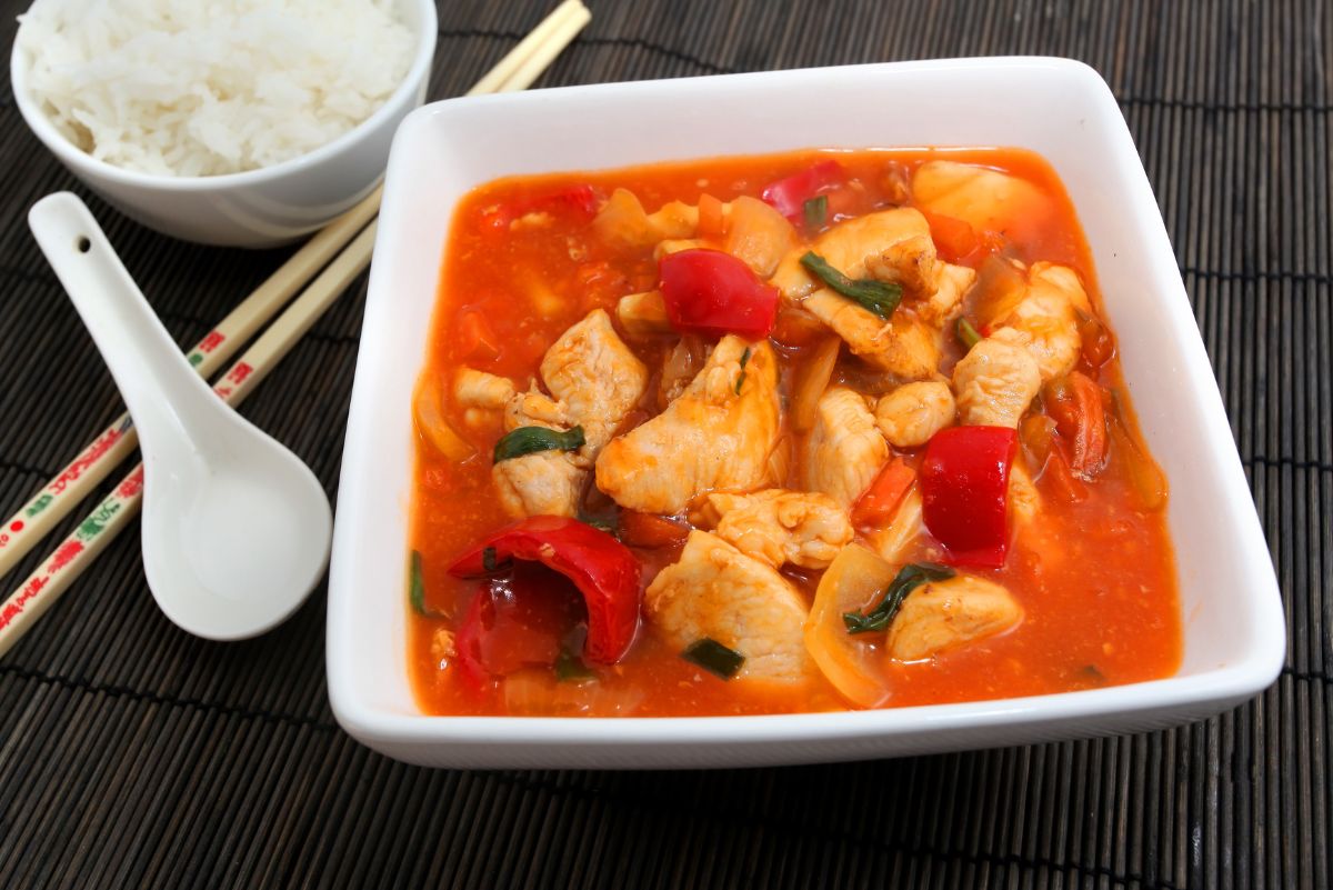 Weight Watchers Slow Cooker Sweet & Sour Chicken in a square, white bowl with a small bowl of rice next to it.