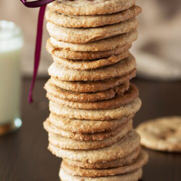 A stack of Weight Watchers Caramel Cookies with a purple bow on top. A glass of milk is partially visible in the background.