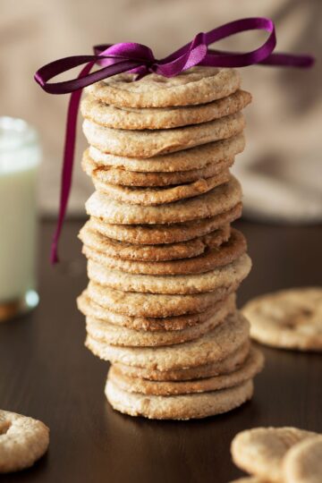 A stack of Weight Watchers Caramel Cookies with a purple bow on top. A glass of milk is partially visible in the background.