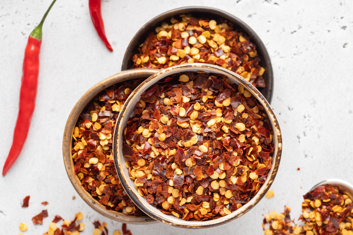 Crushed red pepper flakes in 3 bowls on a white surface.