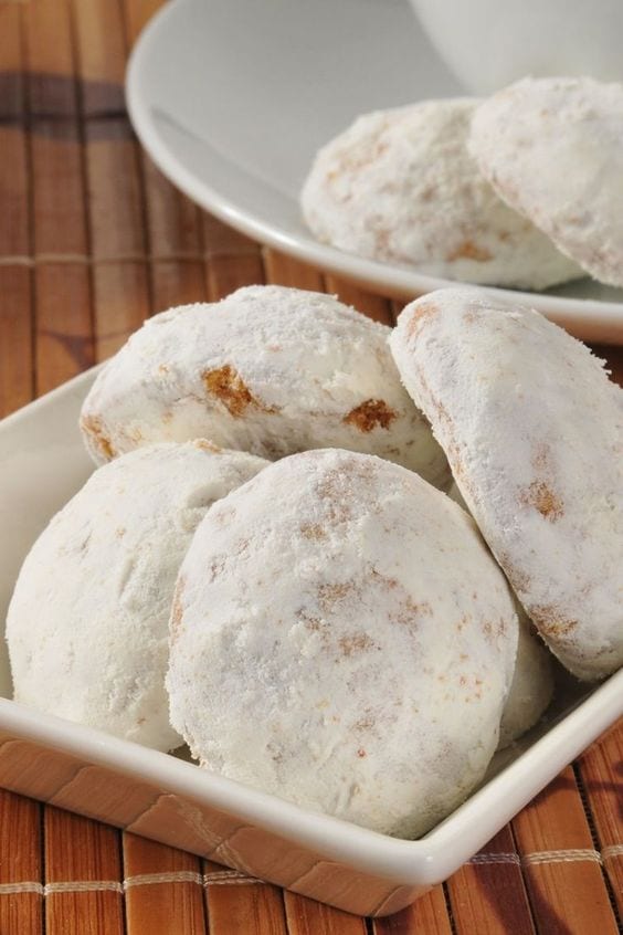 Wedding cookies in a white dish sitting on a wooden table.