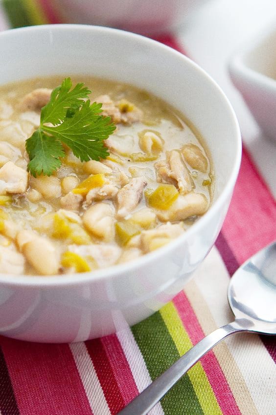 White Chili in a  white bowl, sitting on a colorful stripped placemat with a spoon next to it.