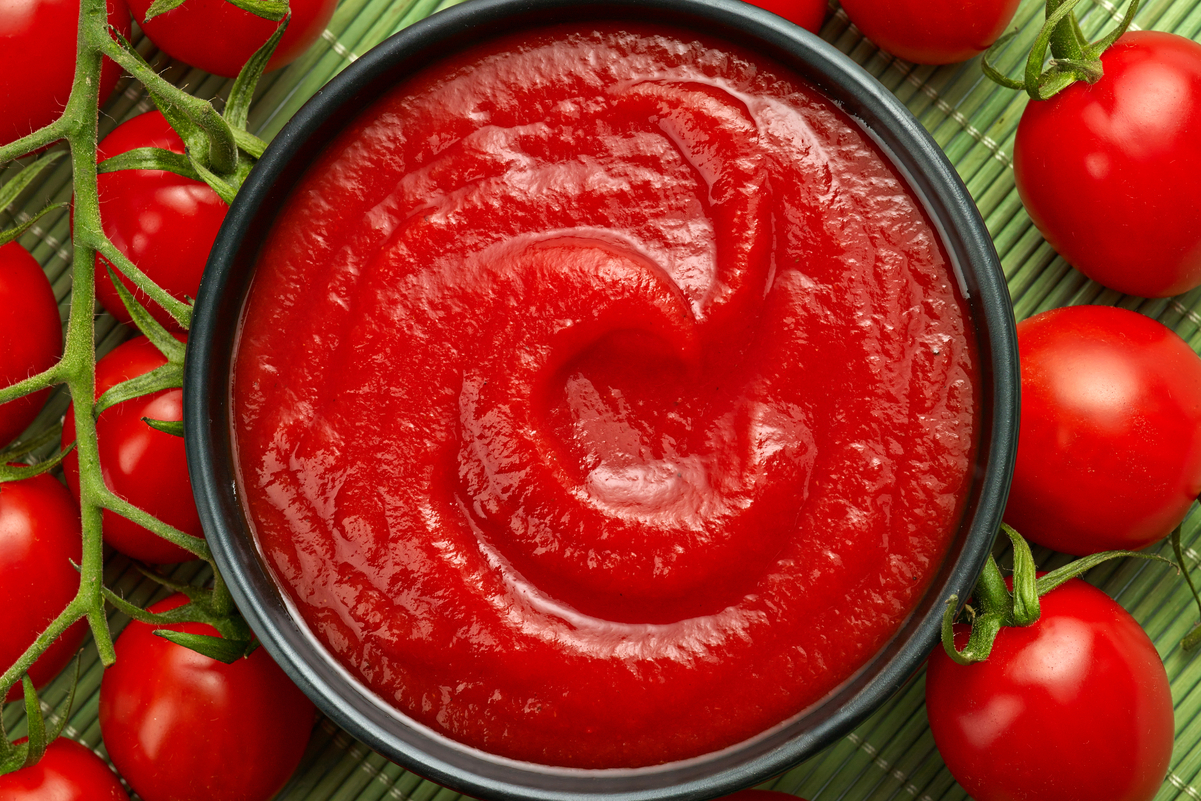 Closeup of tomato sauce in a bowl, surrounded by tomatoes.