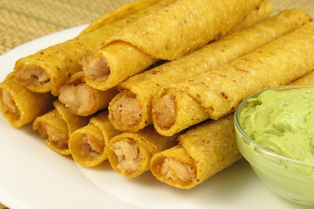 Weight Watchers Chicken and Cheese Taquitos on a white plate with a small glass bowl of guacamole.