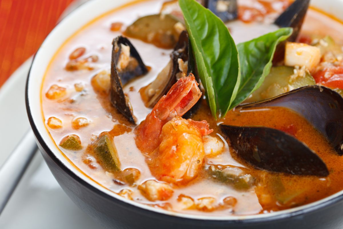 San Francisco style cioppino seafood stew served in a black bowl, with shrimp, mussels, and chunks of white fish in a rich tomato-based broth. Garnished with fresh basil leaves, with visible vegetables and a creamy, savory seafood sauce highlighting a high protein seafood stew.
