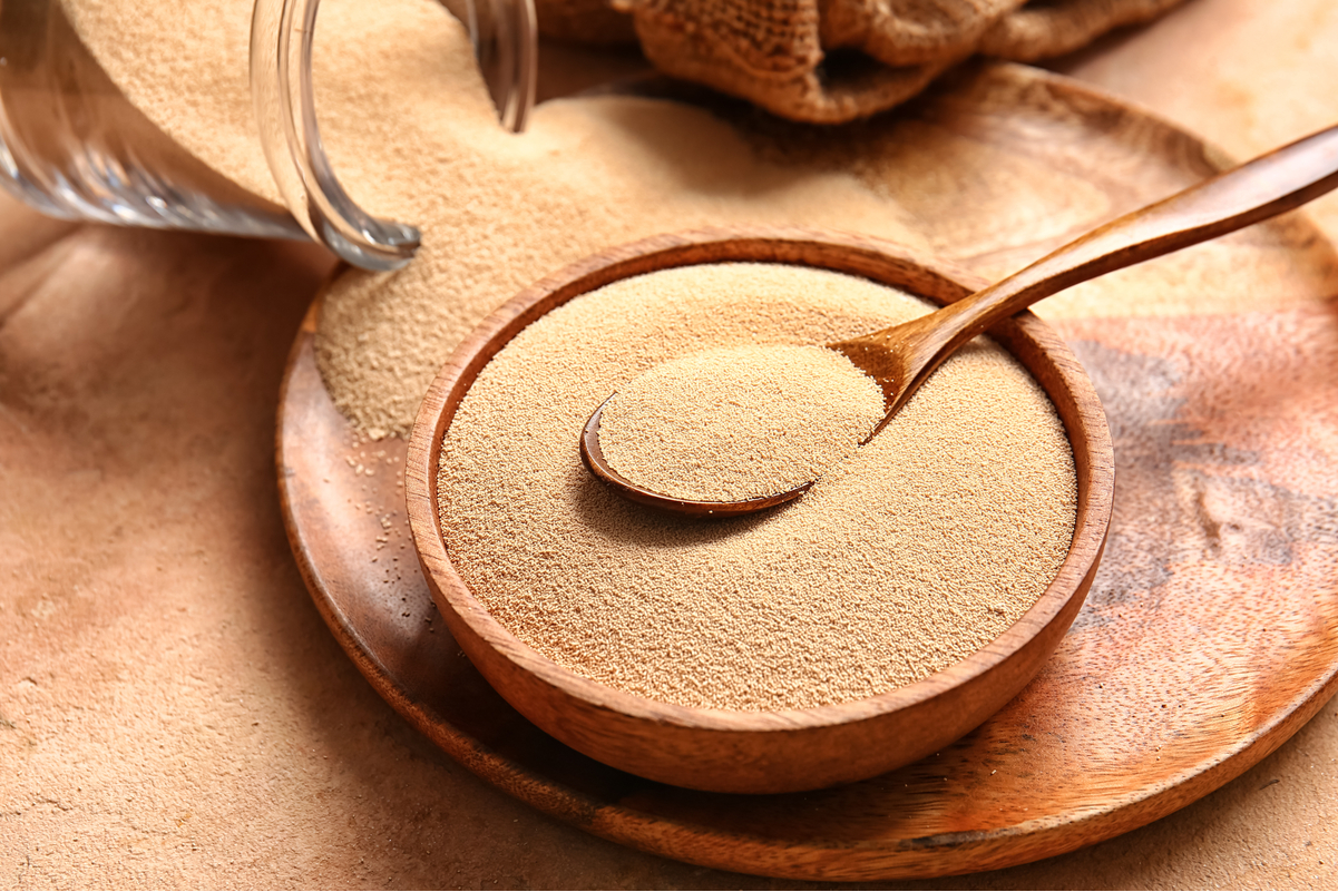 Active dry yeast in a wooden bowl with a spoon in it.