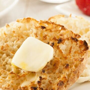 English Muffin on a white plate with strawberries in the background.