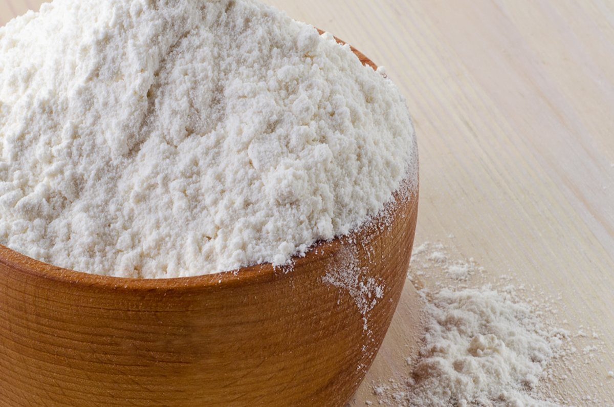 Closeup of flour in a brown bowl sitting on a light colored surface.