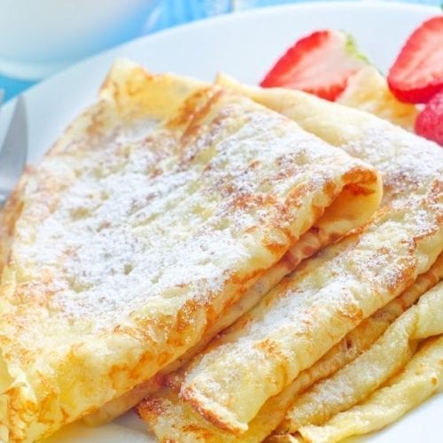 3 Crepes on a white plate with strawberries.