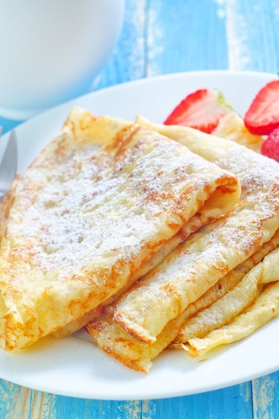 3 Crepes on a white plate with strawberries.