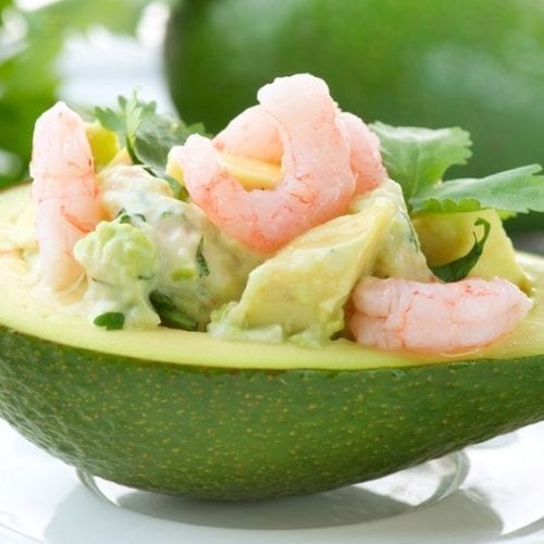 Half of an avocado filled with seafood on a white surface.