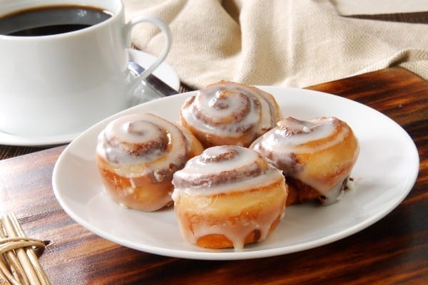 4 Weight Watchers Easy Mini Cinnamon Rolls on a white plate with a cup of coffee in the background.