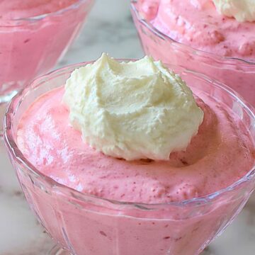 Cherry yogurt Jello fluff served in clear glass dessert cups with whipped topping, showing a creamy pink no-bake dessert on a marble countertop.