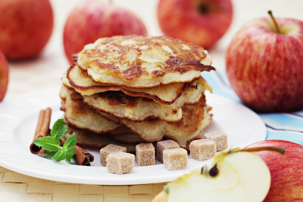 Fall Favorite Cinnamon Apple Pancakes on a white plate that's surrounded by apples.