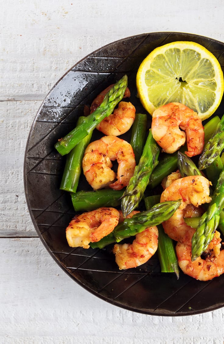 Weight Watchers Garlic Shrimp With Asparagus on a black plate sitting on a rustic light colored wooden surface.