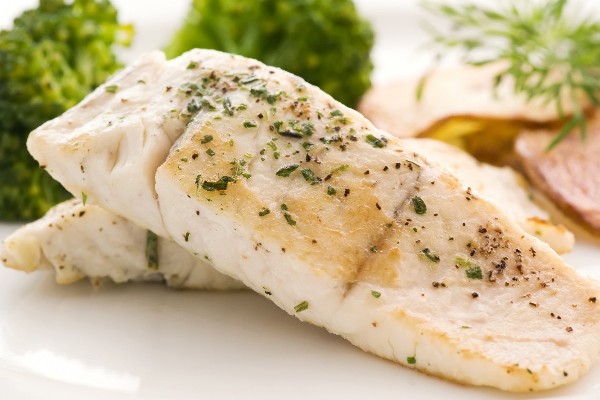 2 pieces of Weight Watchers Herbed Halibut on a white plate with green vegetables in the background.