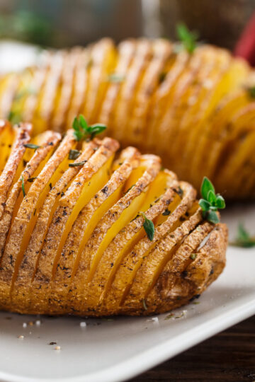 Closeup of WW Air Fryer Hasselback Potatoes on a white plate with an out of focus background.