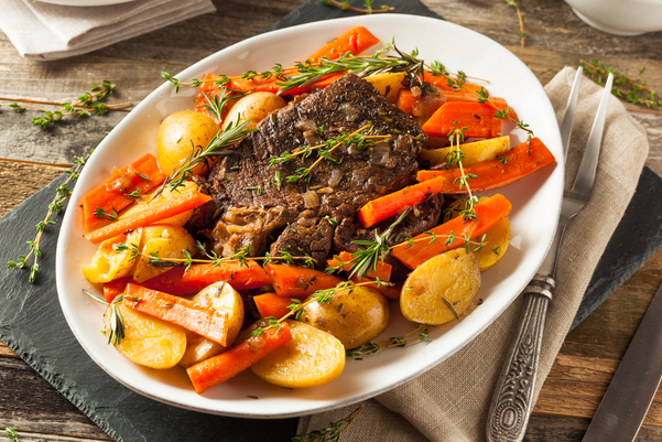 Yankee Pot Roast on a white platter surrounded by carrots and potatoes.