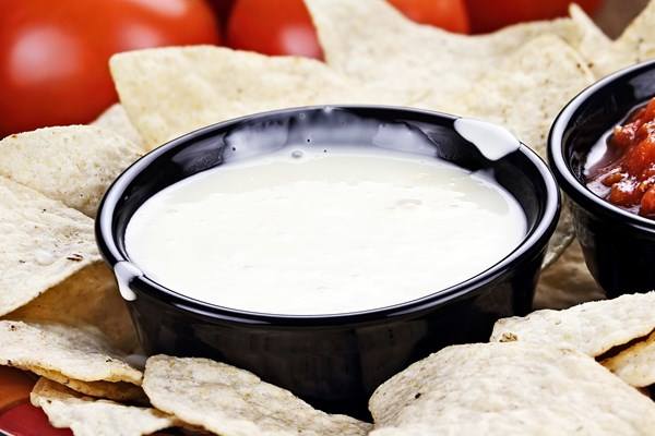 Weight Watchers Mexican Queso Blanco Dip in a black bowl, surrounded by tortilla chips, with tomatoes in the background.