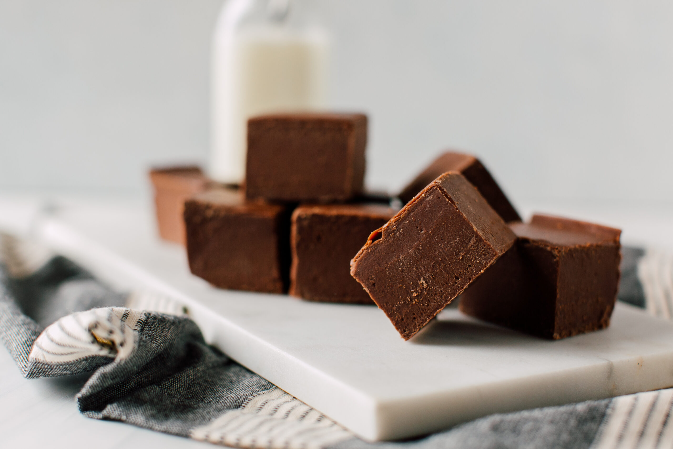 Weight Watchers Healthy Chocolate Fudge on a white cutting board with a dish towel under it. A clear glass bottle of milk out of focus in the background.