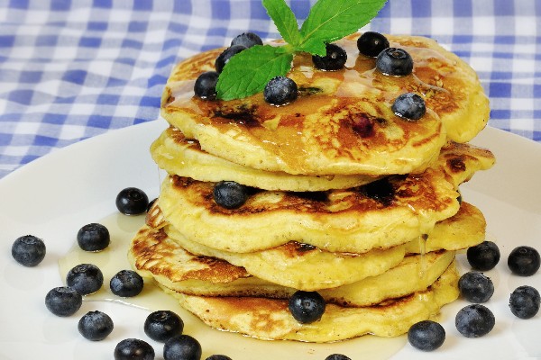A stack of whole wheat blueberry pancakes on a white plate with fresh blueberries.