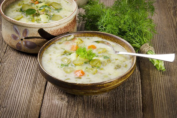 A bowl of Weight Watchers Polish Dill Pickle Soup with a spoon in it and a bunch of dill next to it.