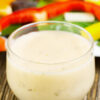 Weight Watchers Copycat Olive Garden Italian Salad Dressing in a glass with out of focus vegetables behind it.