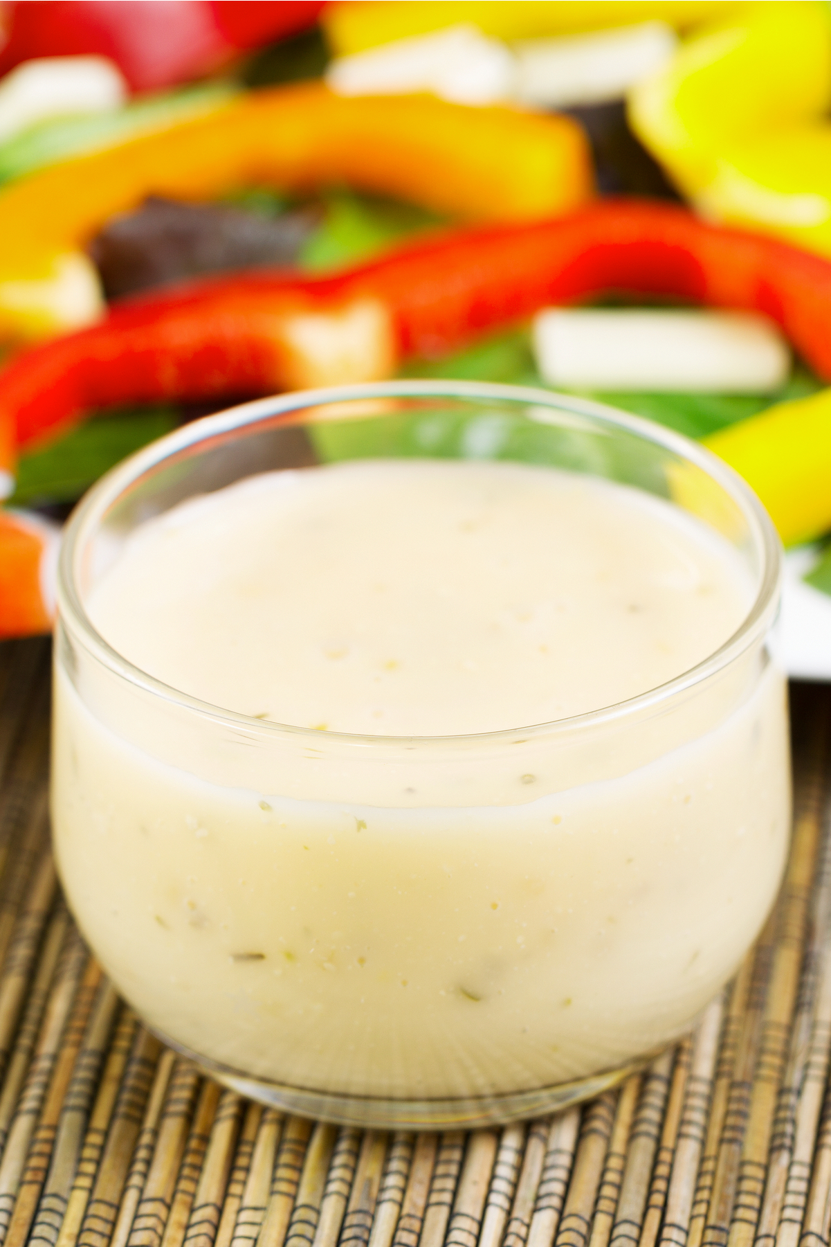 Weight Watchers Copycat Olive Garden Italian Salad Dressing in a glass with out of focus vegetables behind it.