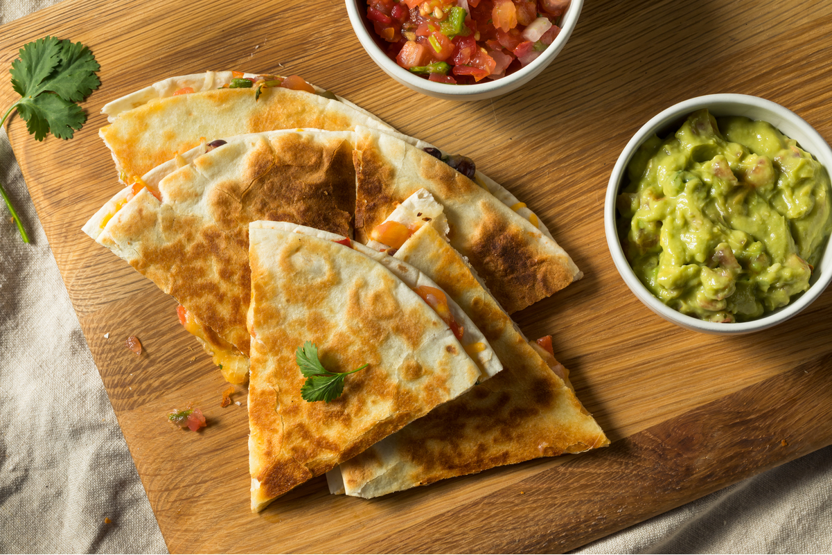 Weight Watchers Vegetable Quesadilla on a wooden cutting board with a small white dish of guacamole.