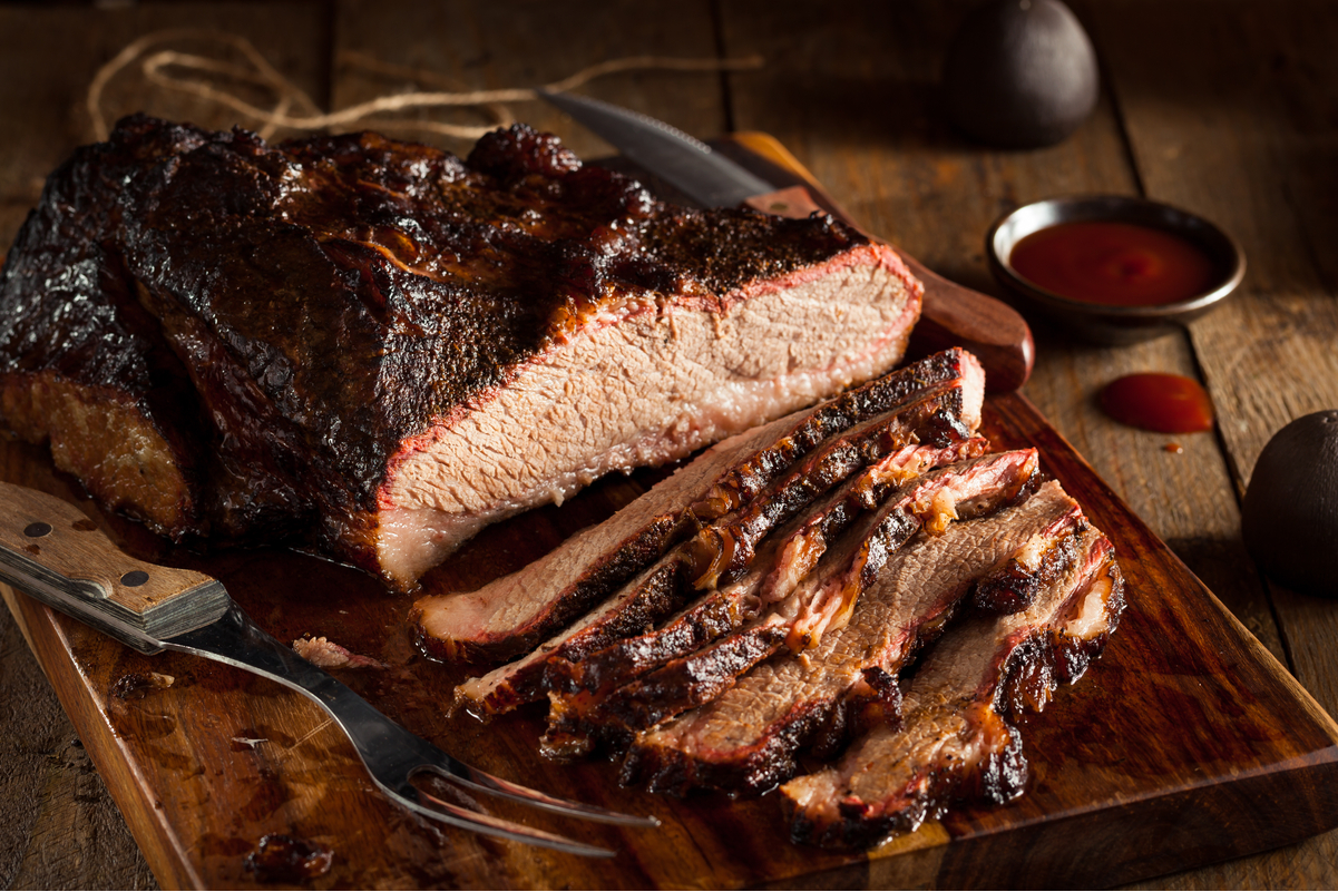 Half sliced Brisket on a wooden cutting board with a fork next to it.