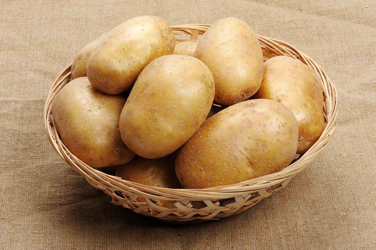 Raw potatoes in a round basket, sitting on a tan surface.