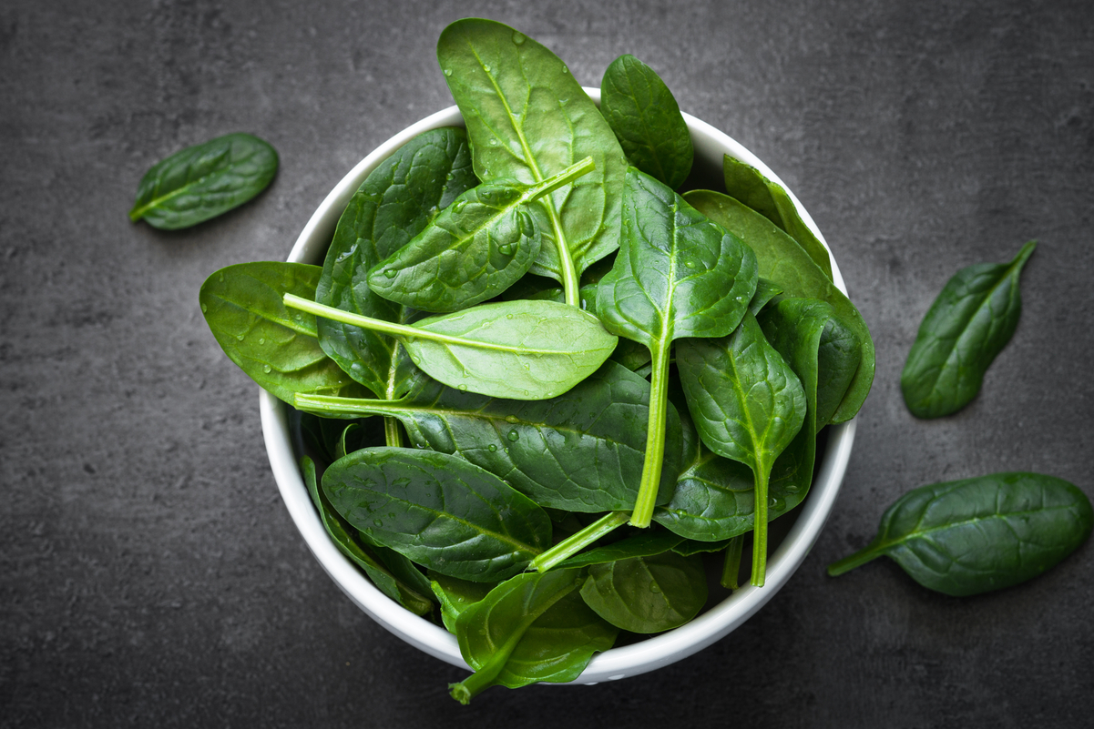 Raw baby spinach in a white dish sitting on a black surface.
