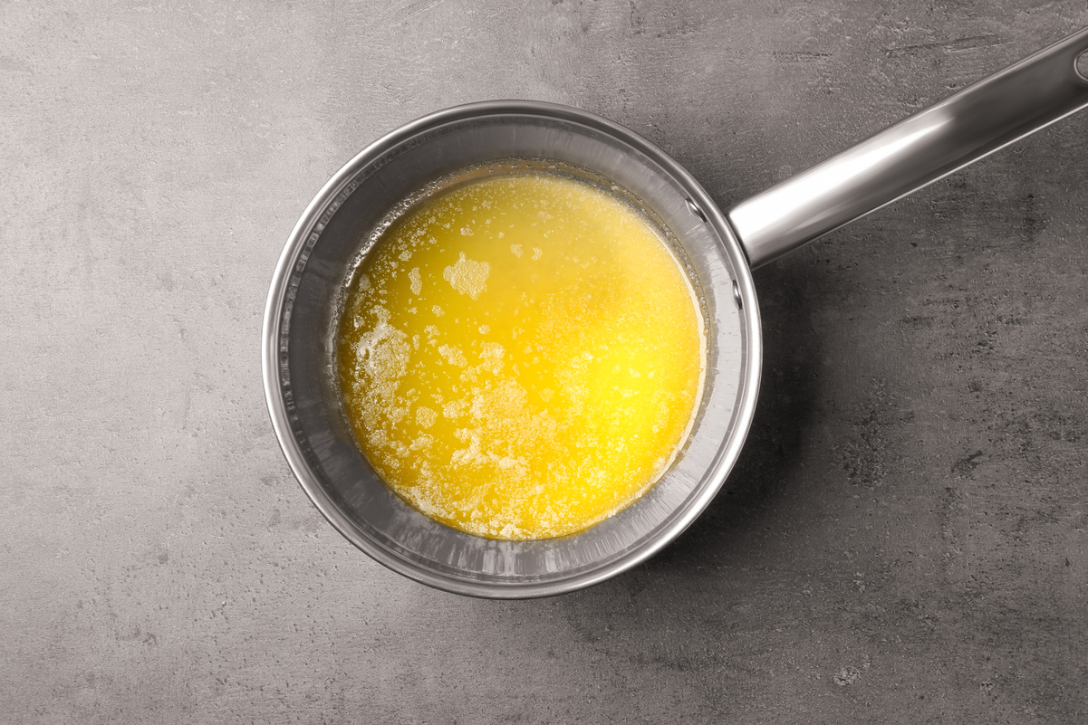 Melted butter in a silver saucepan on a dark gray surface.