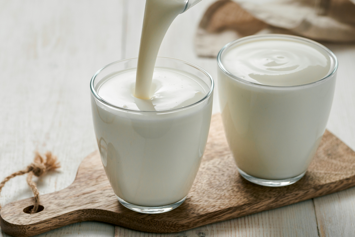 Two glasses of buttermilk sitting on a cutting board.