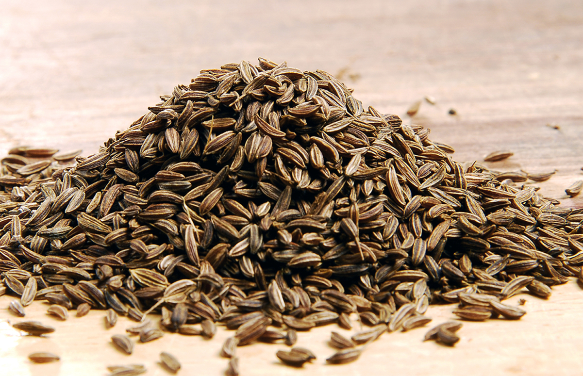 A pile of caraway seeds on a light wooden surface.