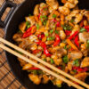 Closeup of Best Weight Watchers Kung Pao Chicken in a black pot with chopsticks resting on it.