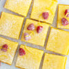 Weight Watchers Lemon Cheesecake Bars on a white surface, with raspberries on top.