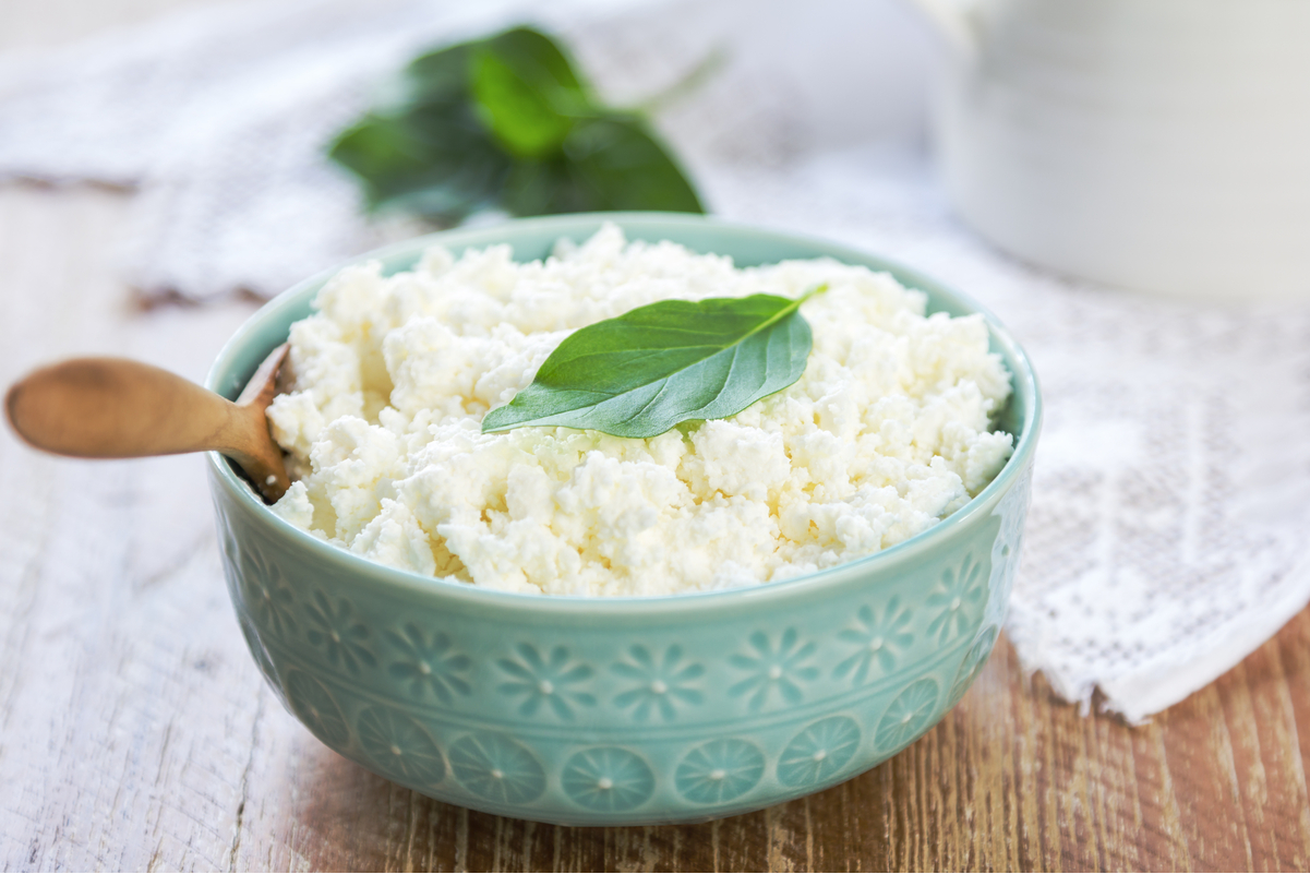 Ricotta cheese in a green bowl, sitting on a wooden surface.