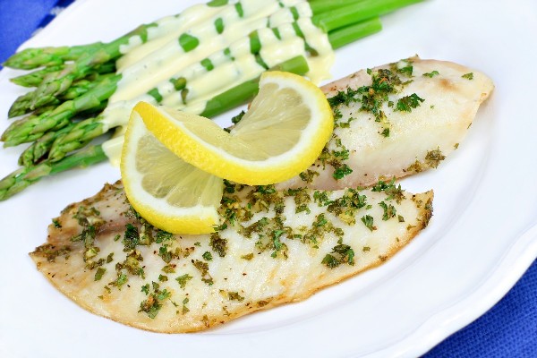 2 pieces of Weight Watchers Lemon Garlic Tilapia on a white plate with asparagus in the background.