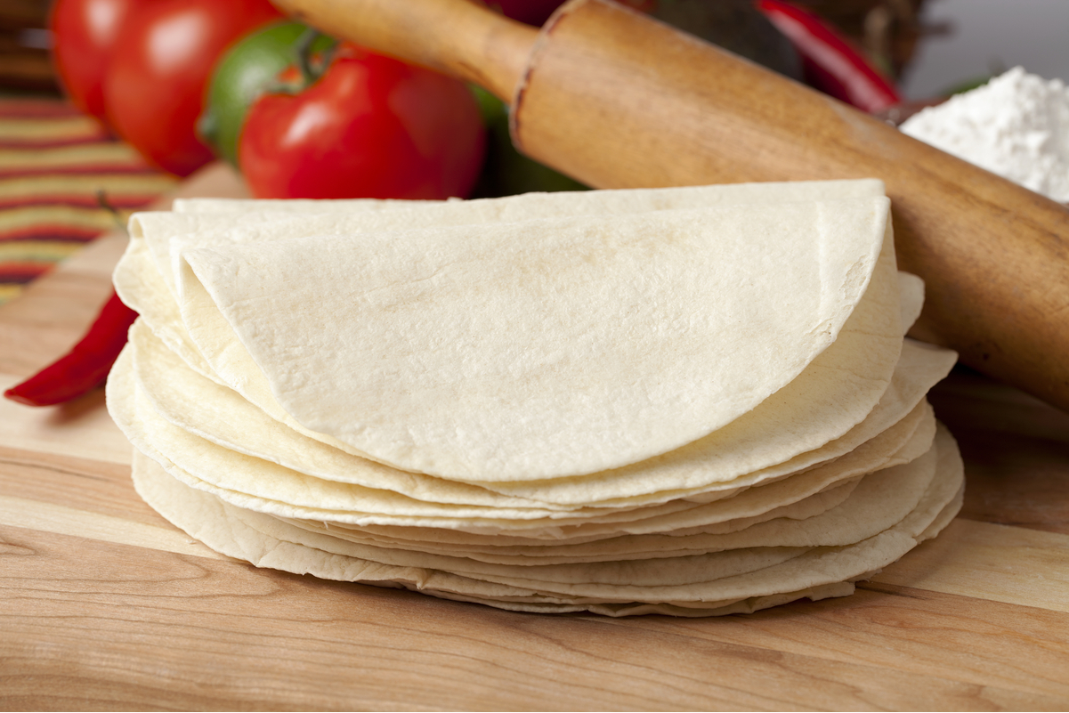 A stack of flour tortillas folded in half on a wooden cutting board.