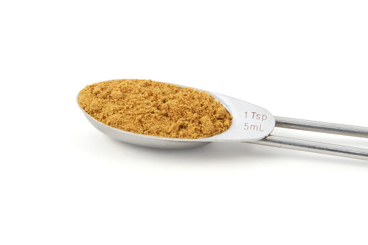 Ground cumin in a measuring spoon on a white background.