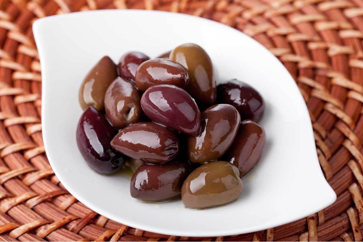 Kalamata Olives in a white dish on a wicker surface.