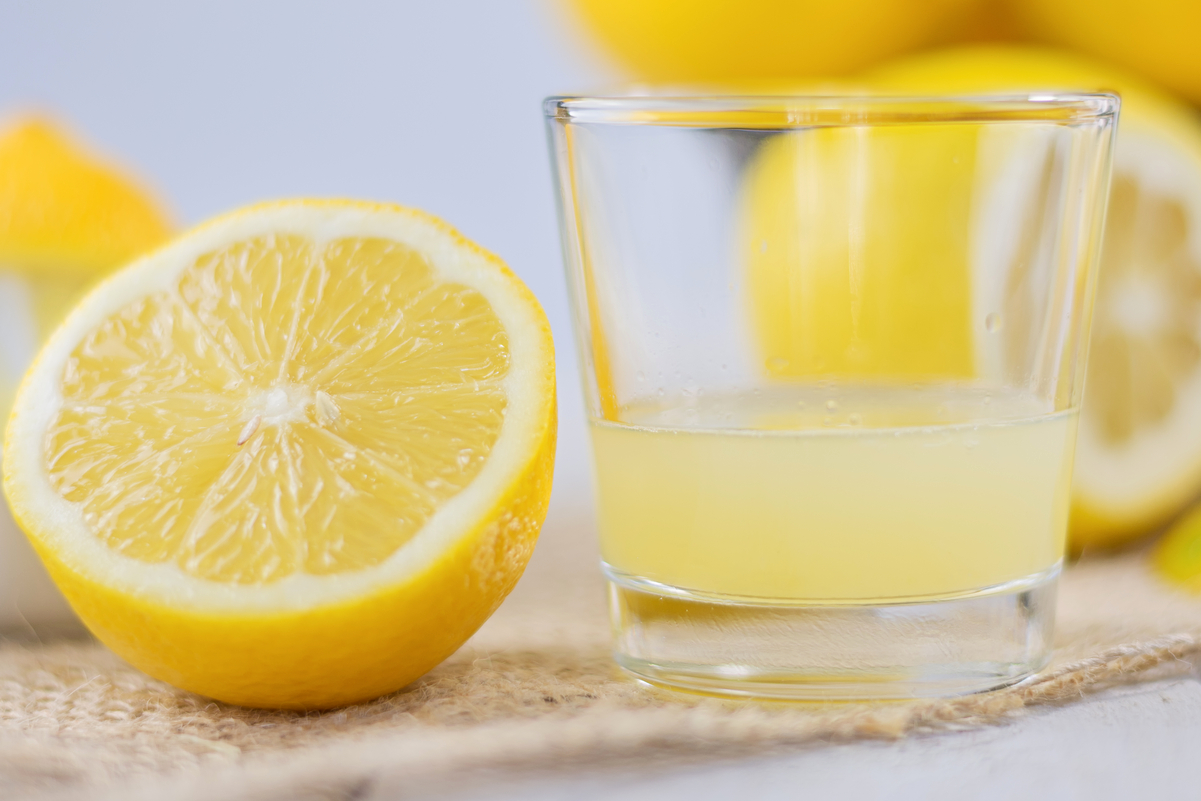 A half lemon next to a clear glass with lemon juice in it.