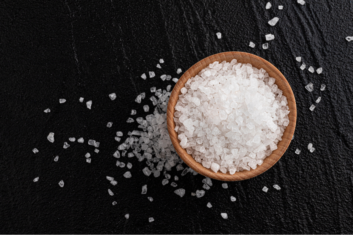 Sea Salt in a brown bowl, on a black surface.