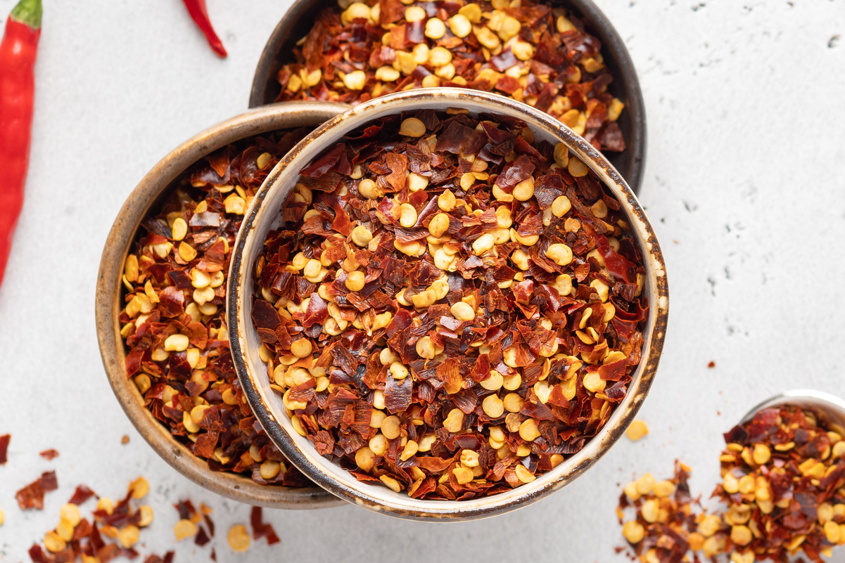 Crushed Red Pepper Flakes in a bowl with a pepper next to it,