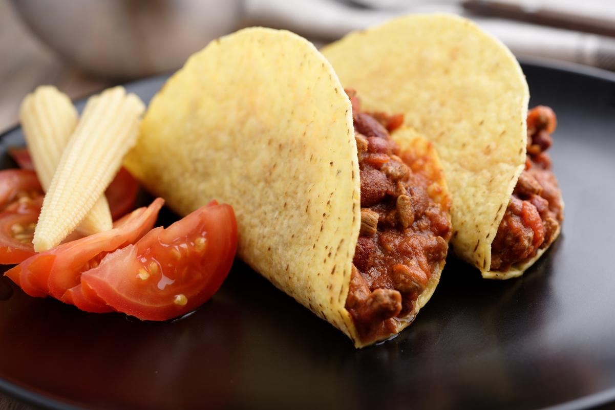 Weight Watchers Ground Beef Chili Tacos on a black plate with wedges of tomato next to them.