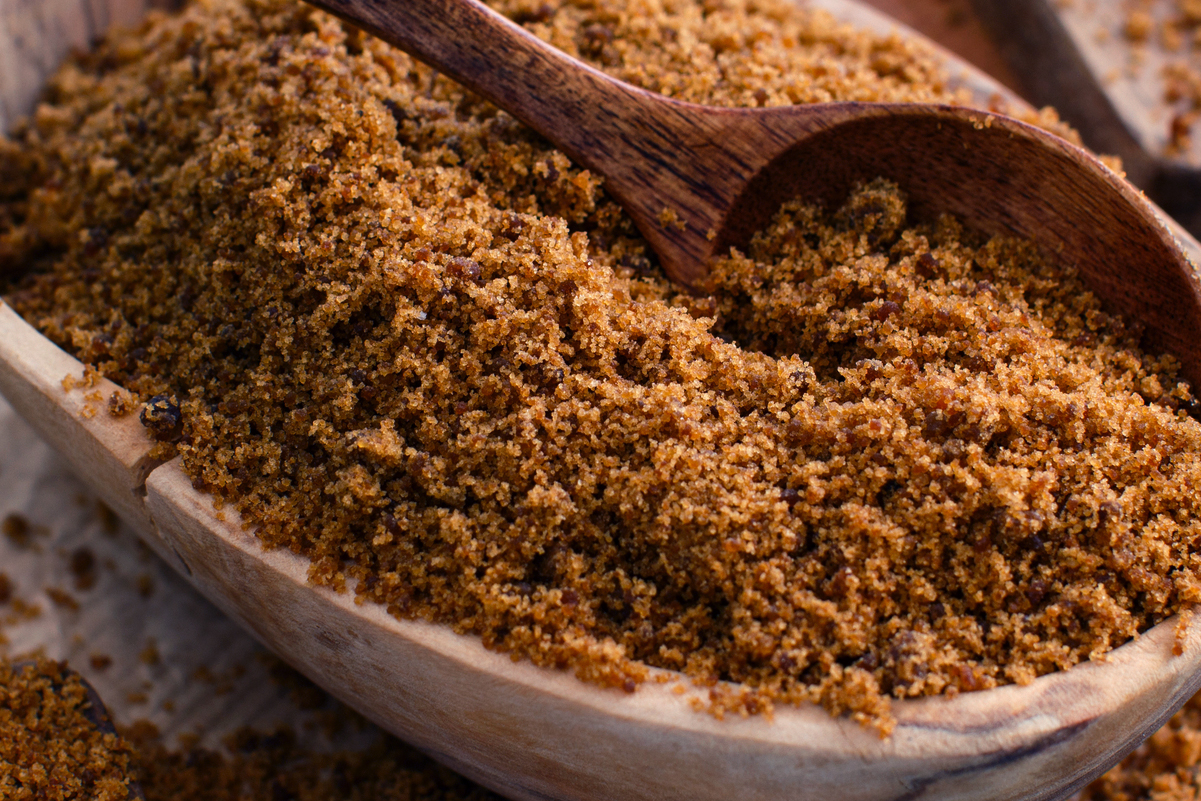 Closeup of a bowl of dark brown sugar with a spoon in it. 